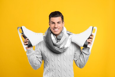 Happy man with ice skates on yellow background