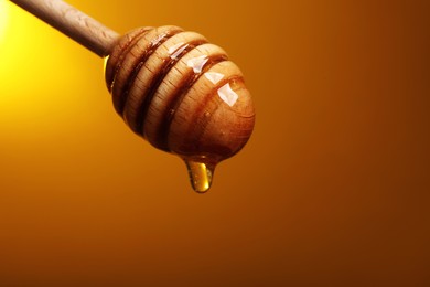 Photo of Pouring honey from dipper against golden background, space for text