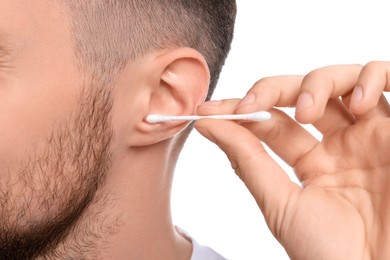 Young man cleaning ear with cotton swab on white background, closeup