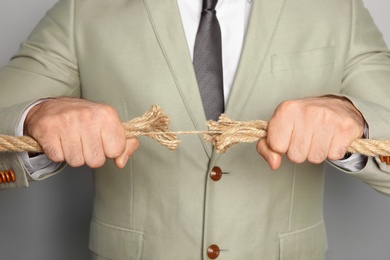 Photo of Businessman pulling frayed rope in opposite directions on gray background