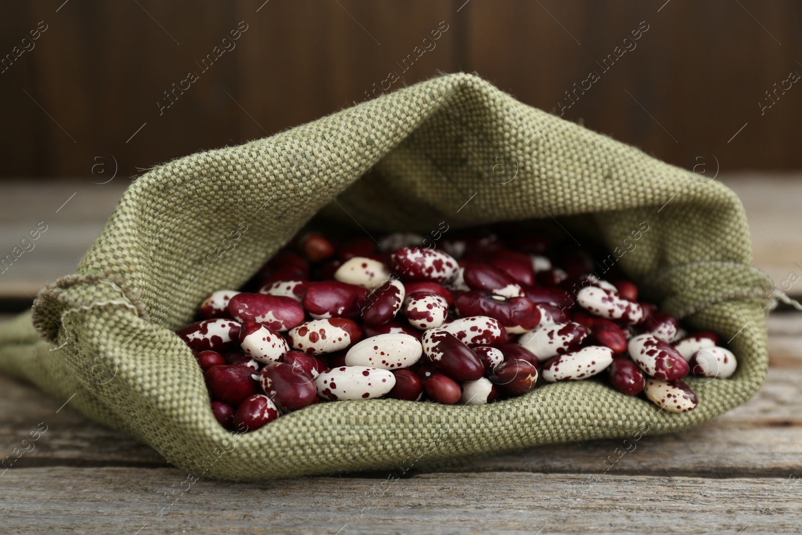 Photo of Overturned sack with dry kidney beans on old wooden table, closeup