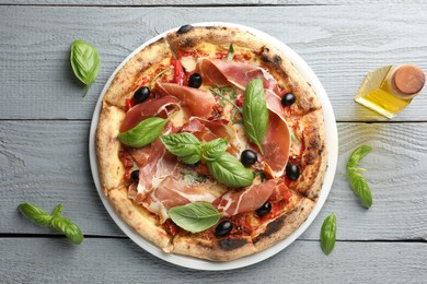 Photo of Tasty pizza with cured ham, olives, sun-dried tomato and basil on gray wooden table, top view