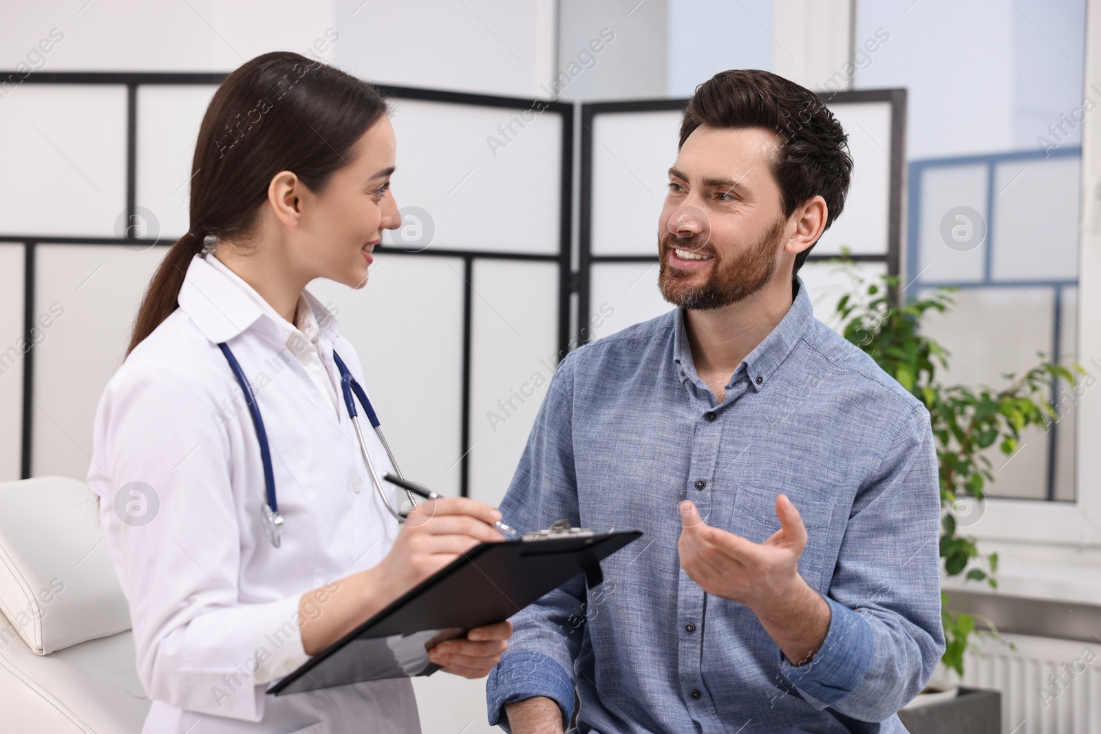 Photo of Doctor with clipboard consulting patient during appointment in clinic