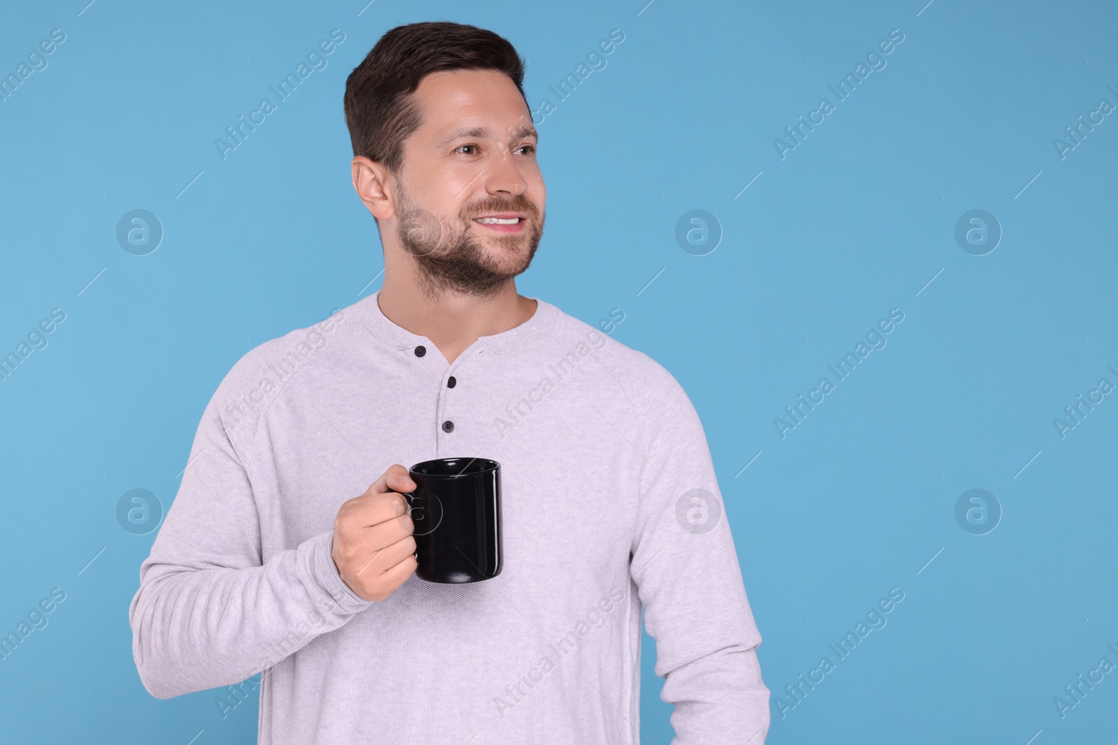Photo of Happy man holding black mug on light blue background. Space for text