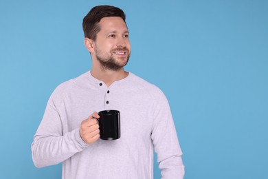 Happy man holding black mug on light blue background. Space for text