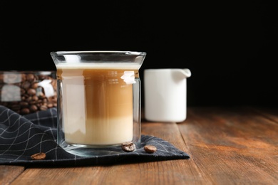 Photo of Composition with glass of delicious coffee drink on wooden table against black background. Space for text