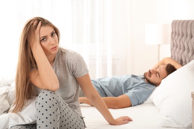 Upset young woman sitting on bed near her sleeping husband at home. Relationship problems