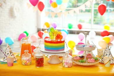 Bright birthday cake and other treats on table in decorated room