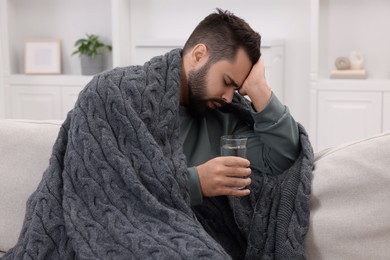 Photo of Man with glass of water suffering from headache on sofa at home