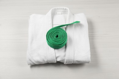 Photo of Green karate belt and white kimono on wooden background, top view