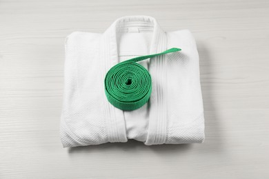 Green karate belt and white kimono on wooden background, top view