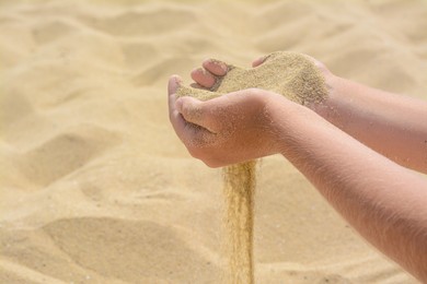 Photo of Child pouring sand from hands on beach, closeup with space for text. Fleeting time concept