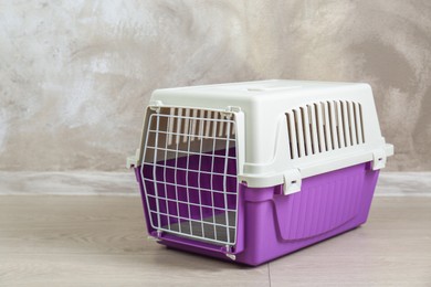 Violet pet carrier on floor near beige wall, space for text