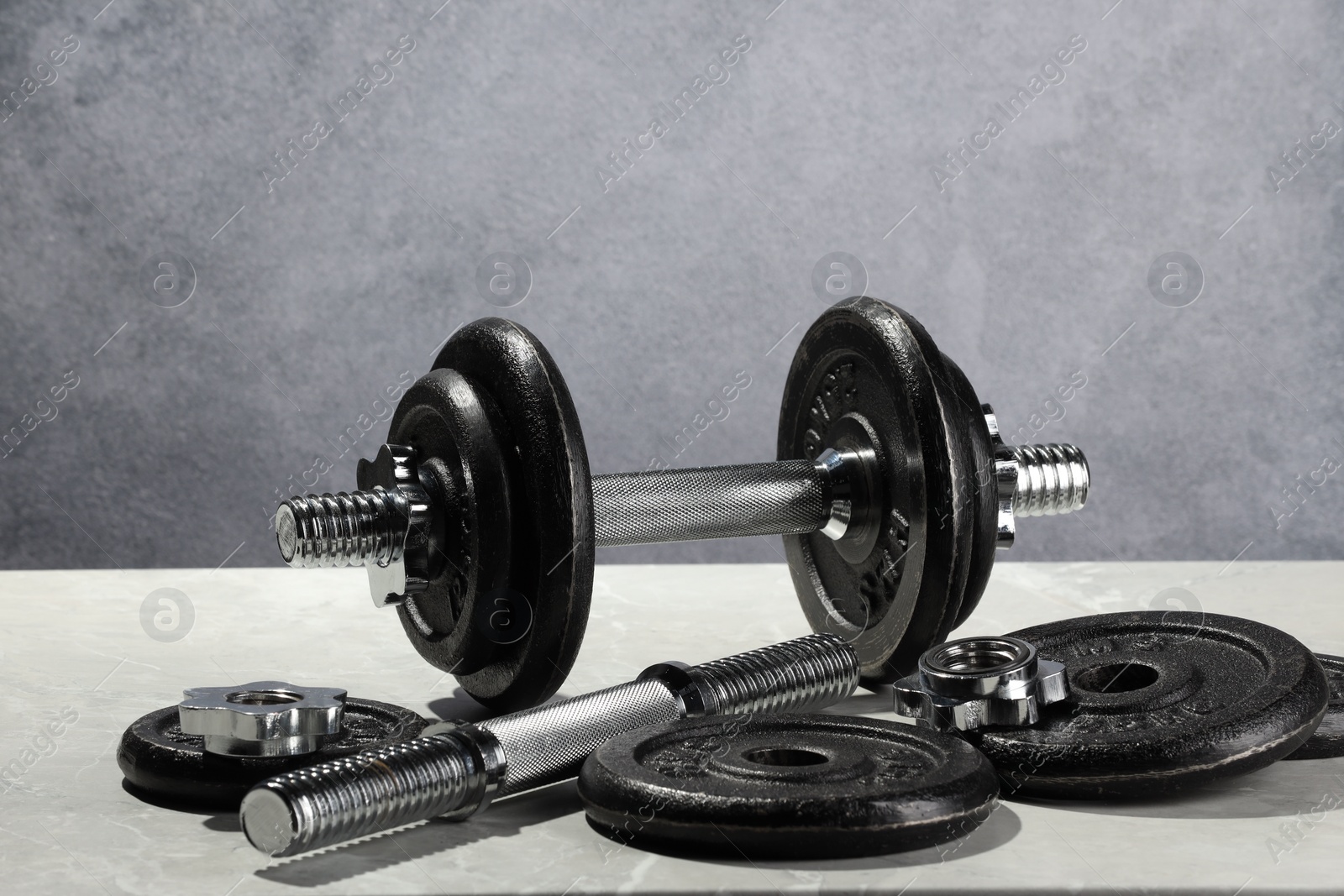 Photo of Barbell and parts of one on light table against grey background