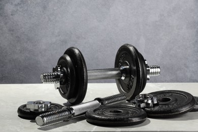 Barbell and parts of one on light table against grey background