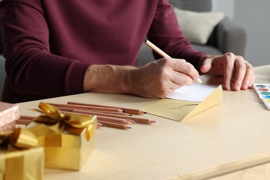 Photo of Man writing message in greeting card at wooden table, closeup