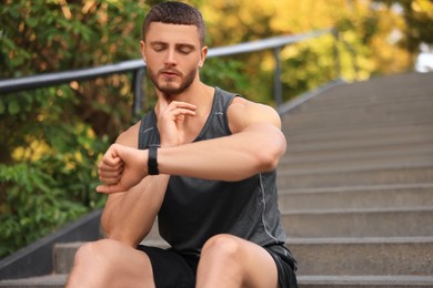 Photo of Attractive serious man checking pulse after training on stairs in park. Space for text