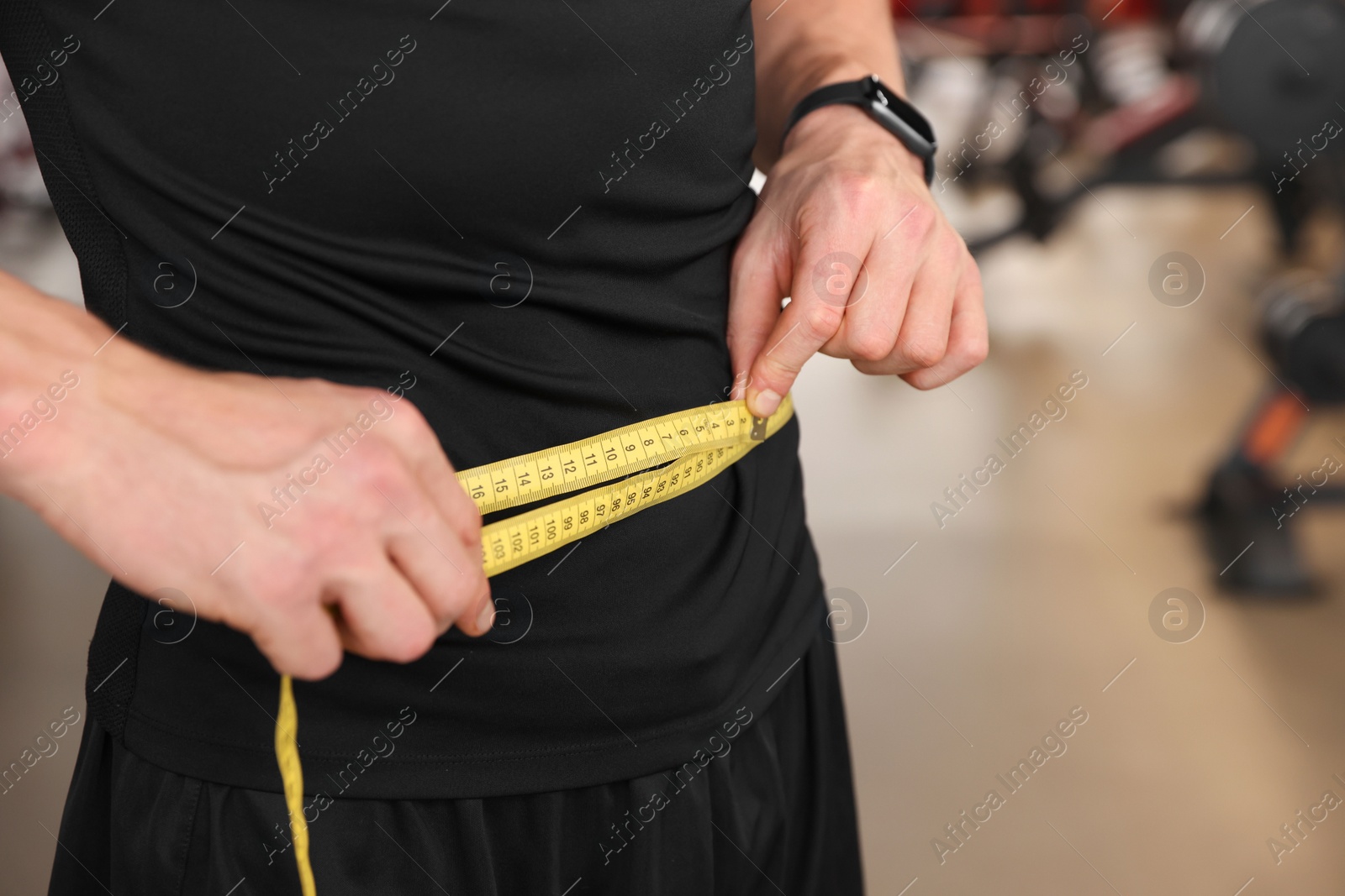 Photo of Athletic man measuring waist with tape in gym, closeup