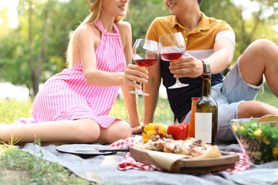 Photo of Happy couple with glasses of wine sitting on lawn, closeup. Summer picnic