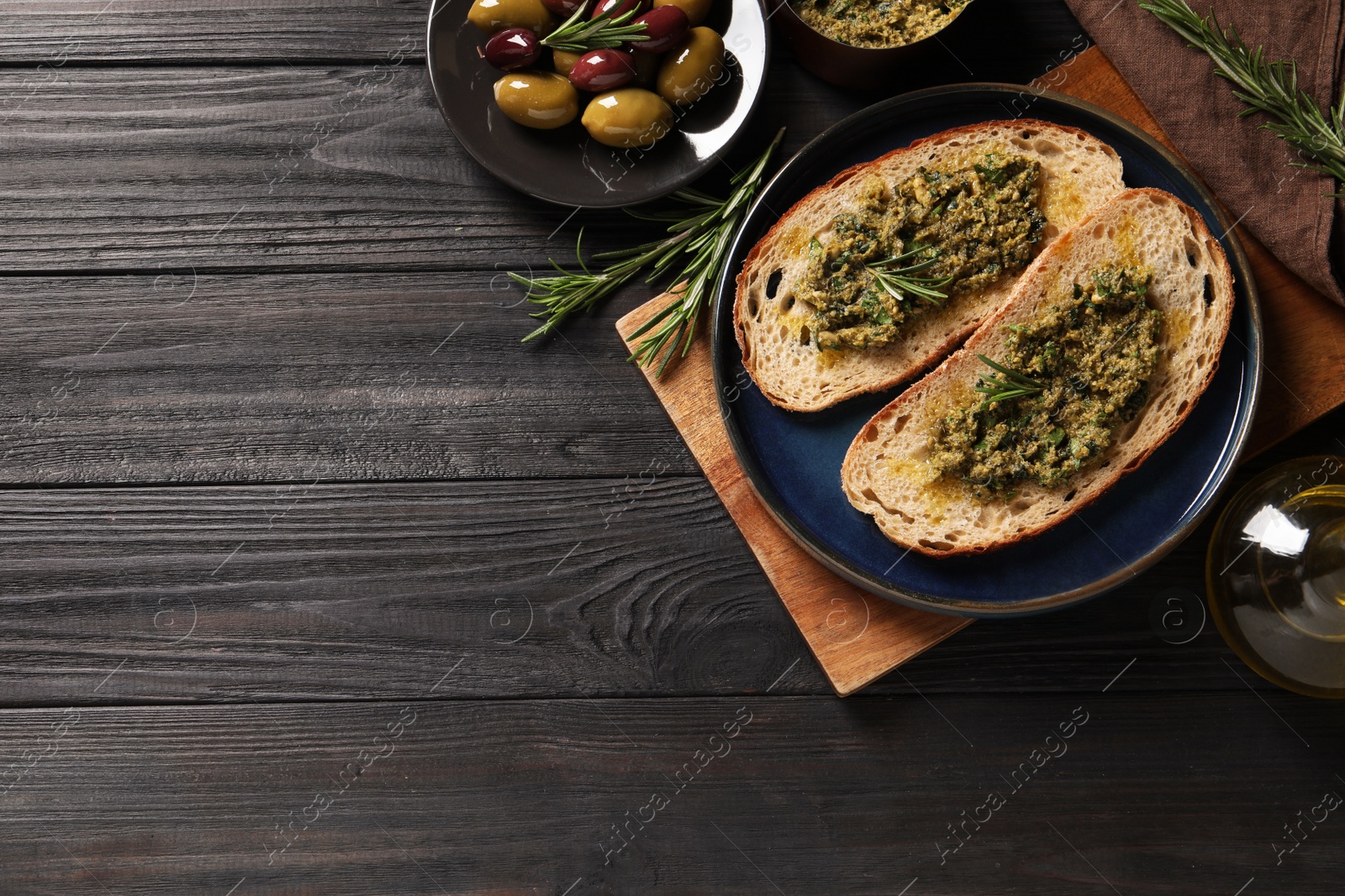 Photo of Tasty bruschettas with pesto and rosemary on black wooden table, flat lay. Space for text