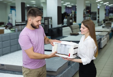 Young saleswoman showing sample of modern orthopedic mattress to customer in store