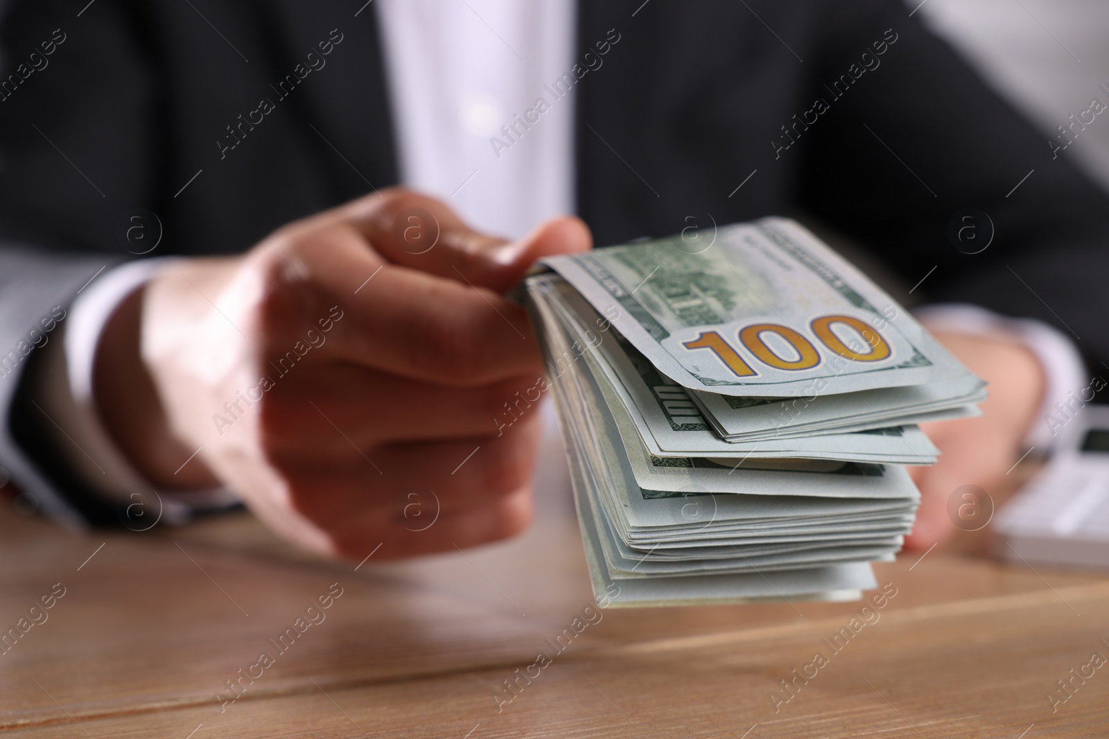 Photo of Money exchange. Man holding dollar banknotes at wooden table, closeup