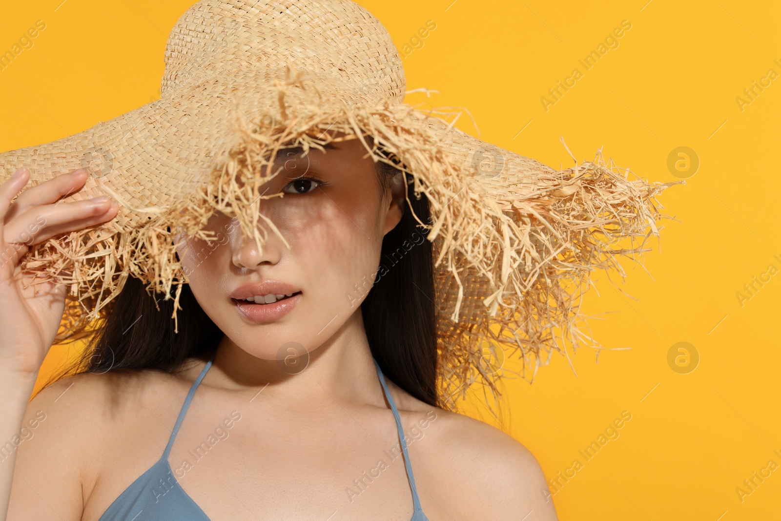 Photo of Beautiful young woman in straw hat on orange background, space for text