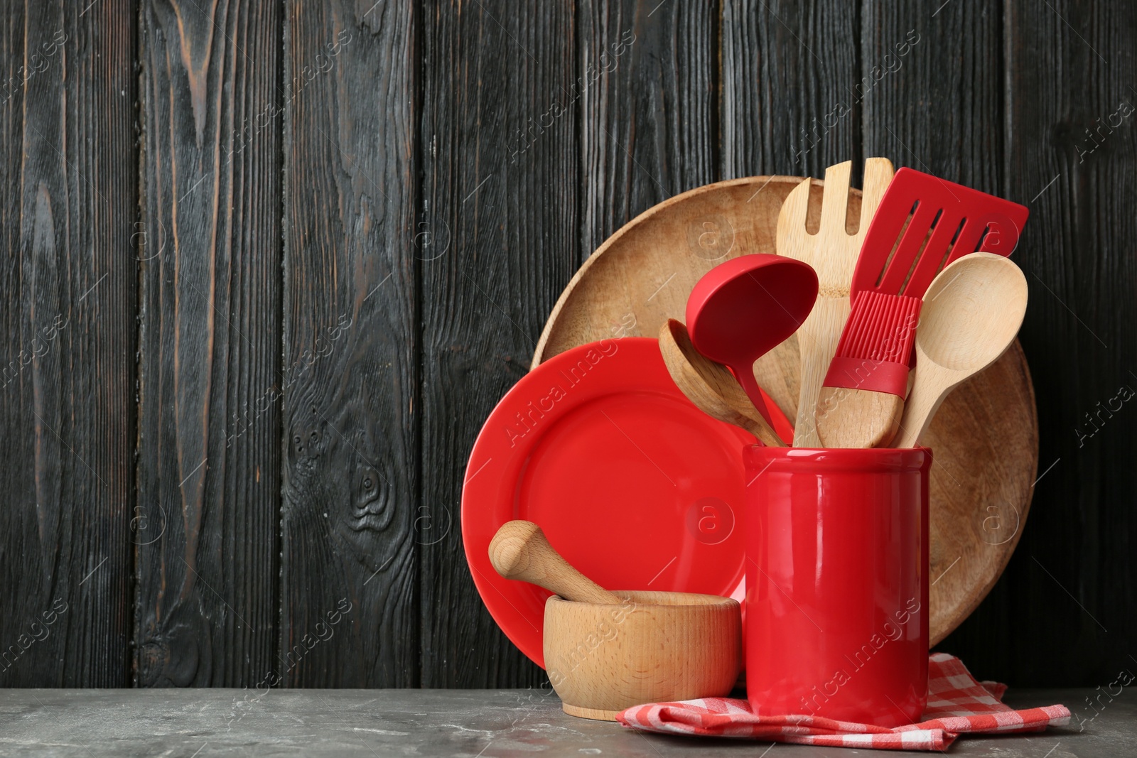 Photo of Different kitchen utensils on grey table against dark wooden background. Space for text