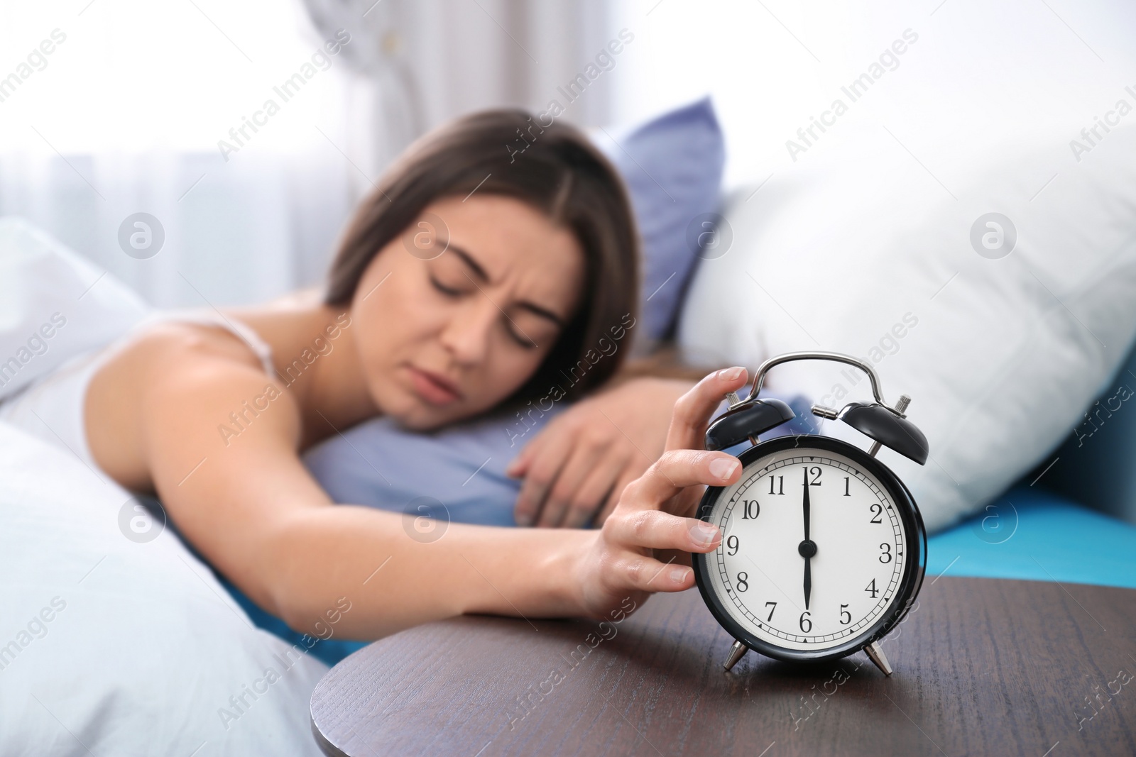 Photo of Young woman turning off alarm clock in morning. Bedtime