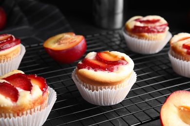 Photo of Delicious cupcakes with plums on black cooling tray, closeup