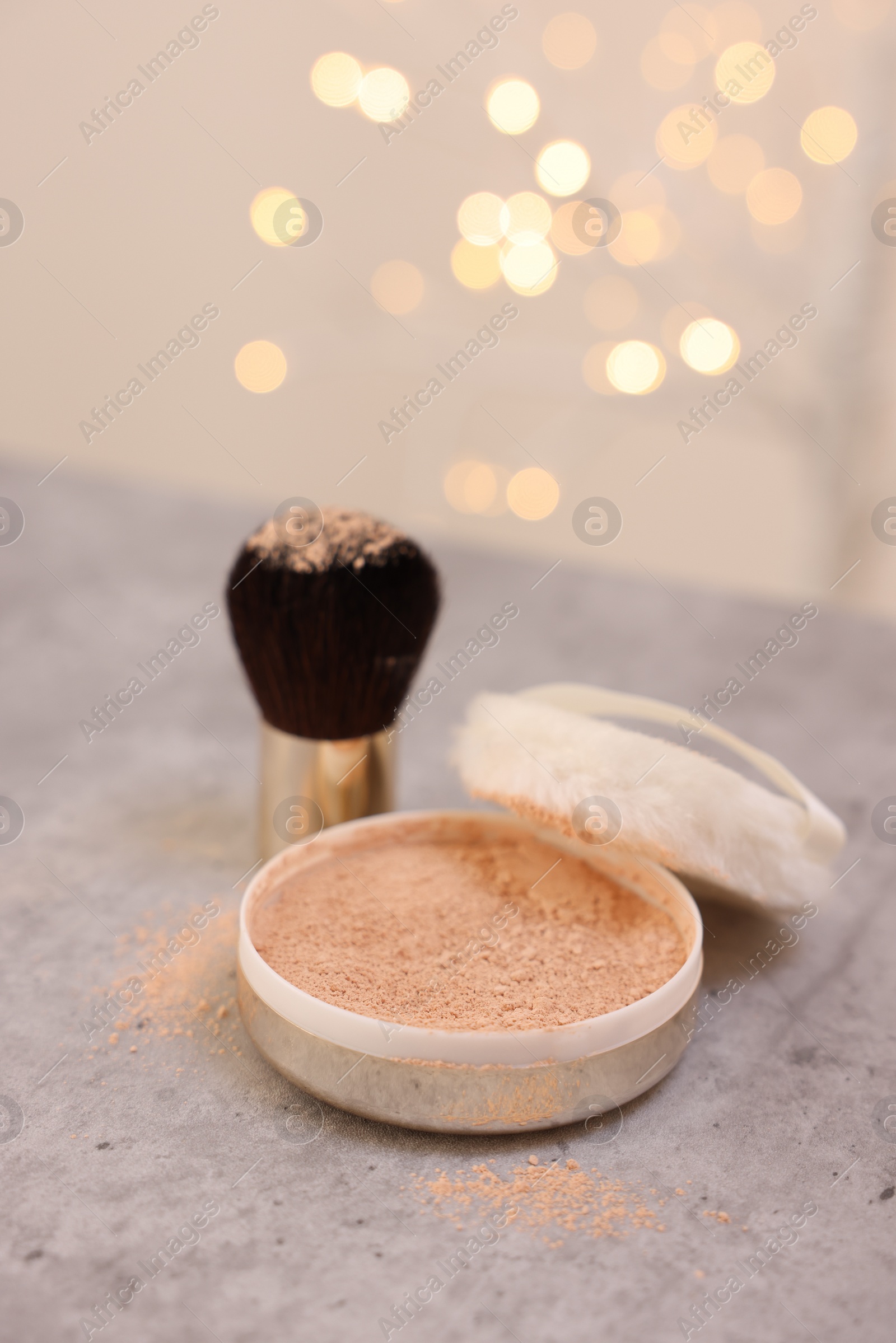 Photo of Face powder and brush on grey textured table against blurred lights