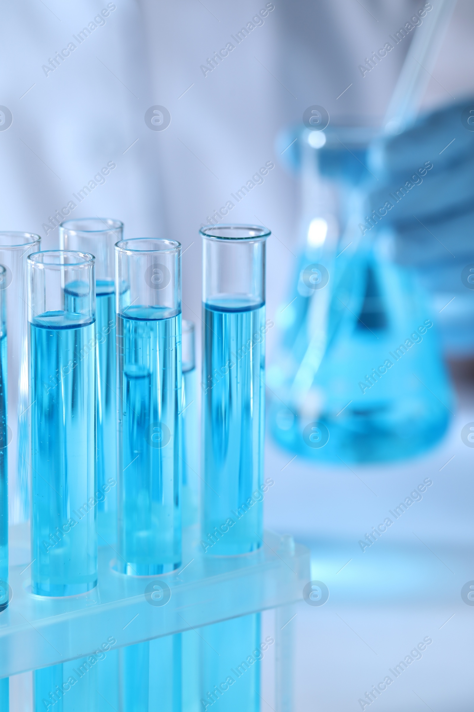 Photo of Scientist holding flask near test tubes with light blue liquid, selective focus