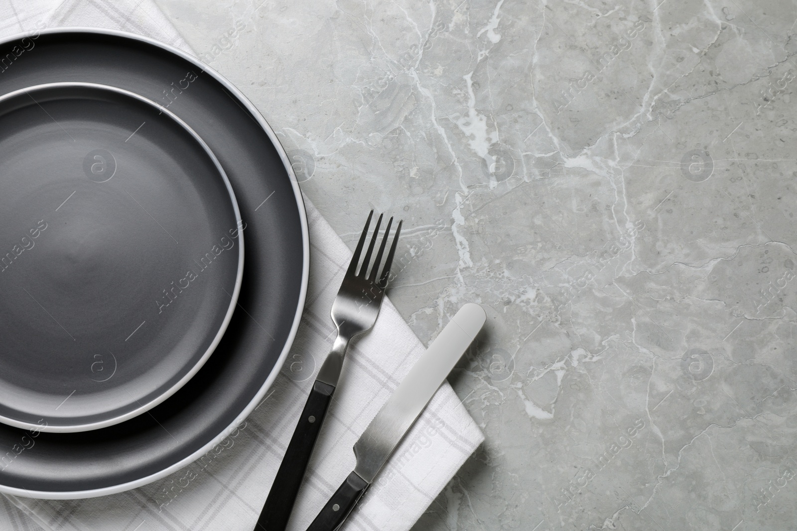 Photo of New dark plates, cutlery and napkin on light grey marble table, flat lay. Space for text