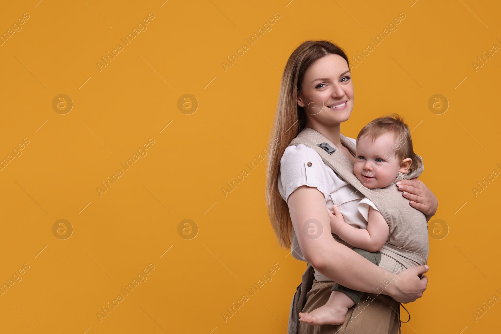 Photo of Mother holding her child in sling (baby carrier) on orange background. Space for text