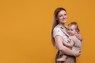 Photo of Mother holding her child in sling (baby carrier) on orange background. Space for text