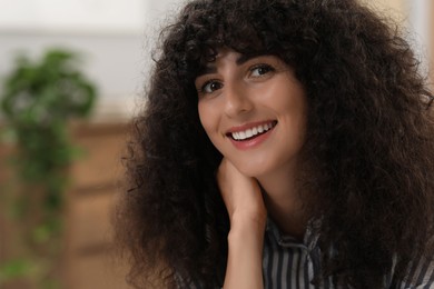 Portrait of beautiful woman with curly hair indoors. Attractive lady smiling and posing for camera. Space for text