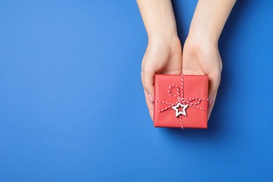 Woman holding beautifully wrapped Christmas gift box on blue background, top view. Space for text