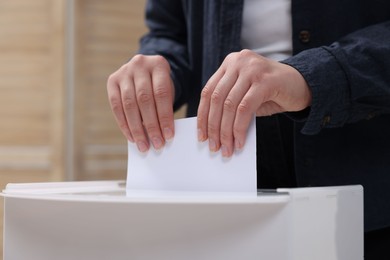 Photo of Woman putting her vote into ballot box on blurred background, closeup