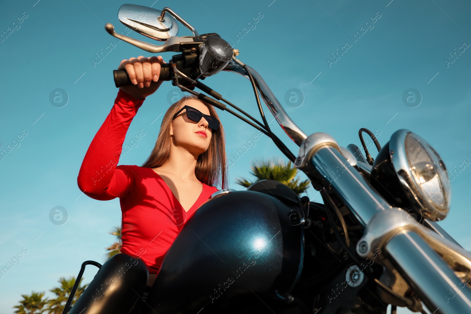 Photo of Beautiful young woman riding motorcycle on sunny day, low angle view