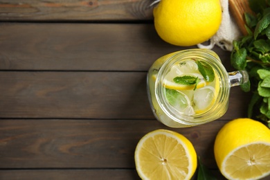 Photo of Mason jar of cold lemonade and ingredients on wooden table, flat lay. Space for text