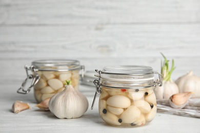 Composition with jars of pickled garlic on white wooden table