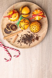 Pomander balls made of tangerines with cloves and candy canes on wooden table, flat lay. Space for text