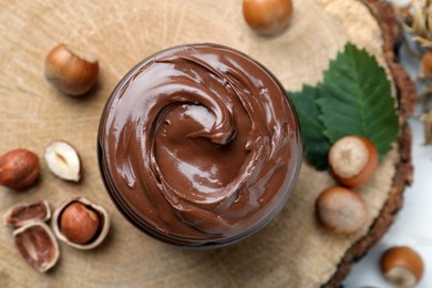 Jar with tasty chocolate spread and hazelnuts on wooden board, flat lay