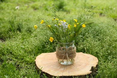 Bouquet of beautiful wildflowers in glass vase on wooden stump outdoors
