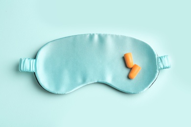 Pair of ear plugs and sleeping mask on turquoise background, flat lay