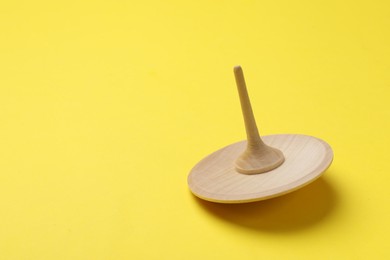 Photo of One wooden spinning top on yellow background, space for text