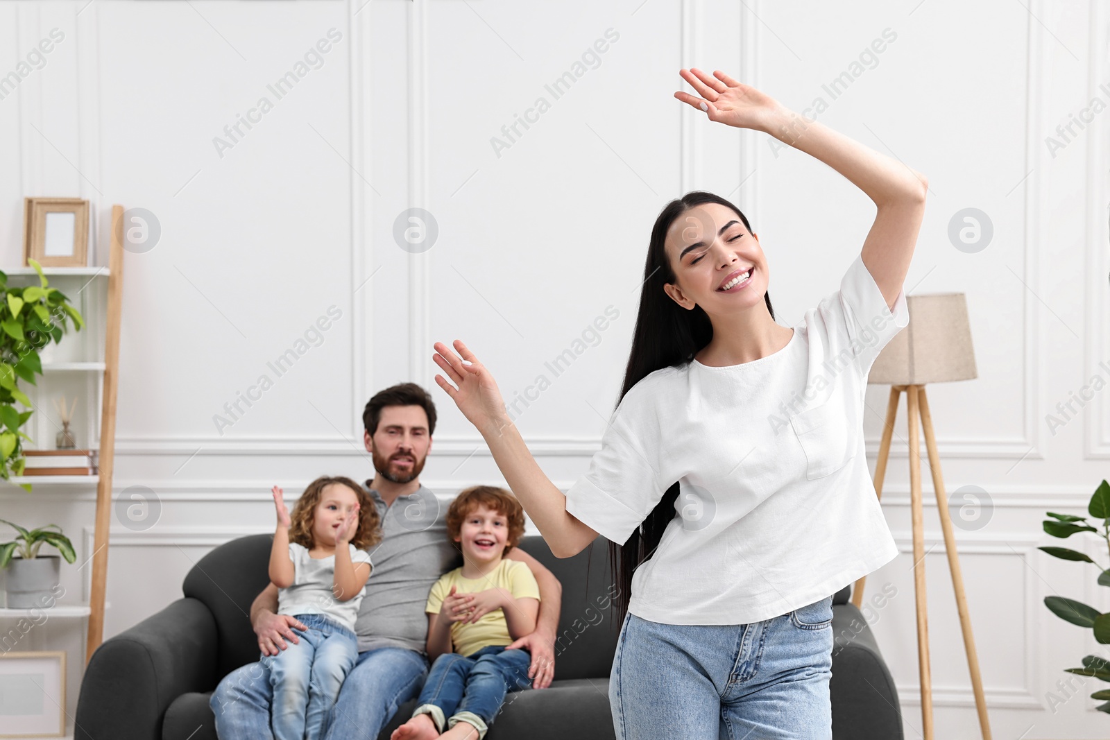 Photo of Happy family having fun at home. Mother dancing while her relatives resting on sofa