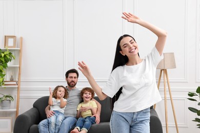 Photo of Happy family having fun at home. Mother dancing while her relatives resting on sofa