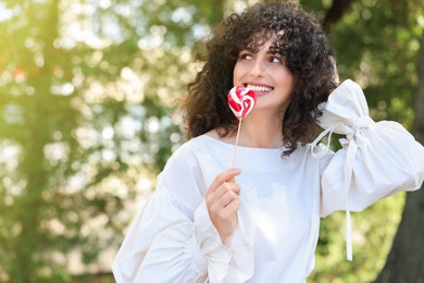 Beautiful woman with lollipop outdoors, space for text