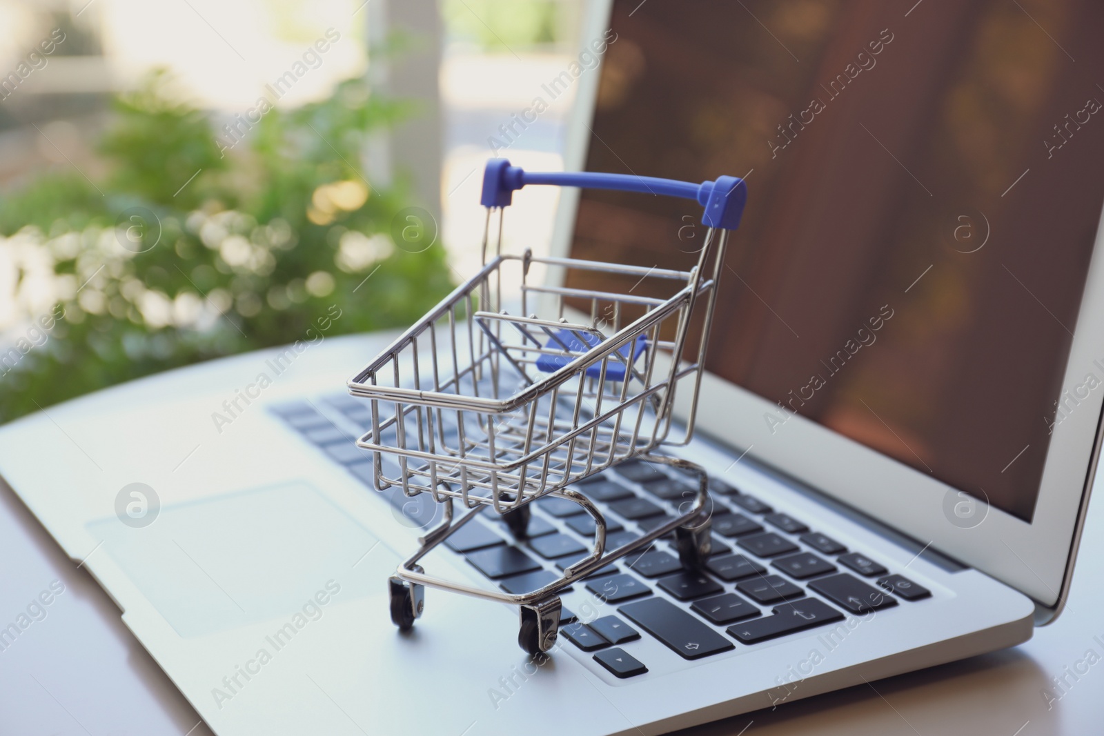 Photo of Internet shopping. Laptop with small cart on table indoors, closeup